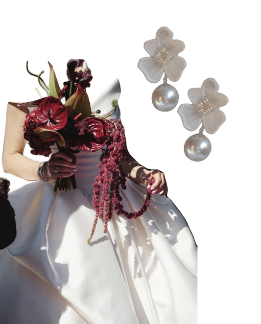 A pair of white lace flower-shaped drop earrings with round pearl drops and small pearl centers, shown beside a bride in a white wedding dress holding a dark red floral bouquet on a white background.